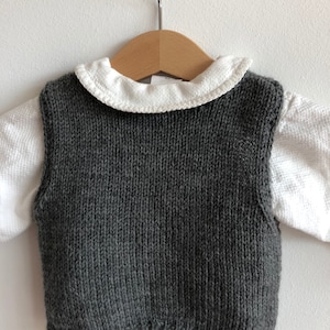 May include: A grey knitted waistcoat with a white collared shirt underneath. The waistcoat is sleeveless and has a ribbed texture.