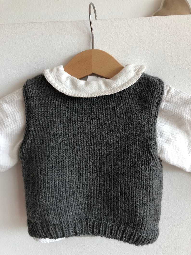 May include: A grey knitted waistcoat with a white collared shirt underneath. The waistcoat is sleeveless and has a ribbed texture.