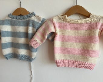 May include: Two striped knitted jumpers, one blue and white, the other pink and white, hanging on wooden hangers.