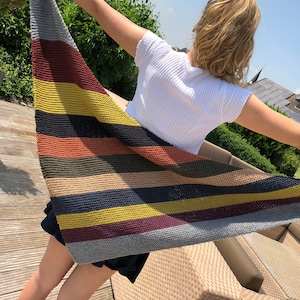 Puede incluir: Un chal triangular a rayas en tonos grises, marrones, amarillos y negros. El chal está tejido con un punto texturizado.