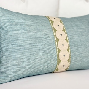 May include: A light blue throw pillow with a decorative green and white trim. The trim features a repeating pattern of circles.