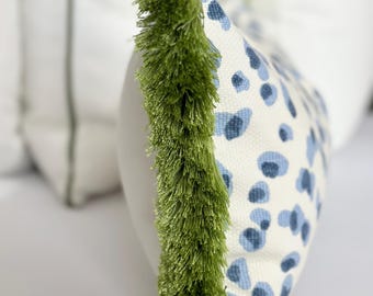 May include: A white pillow with a blue and white abstract pattern and a green fringe trim.
