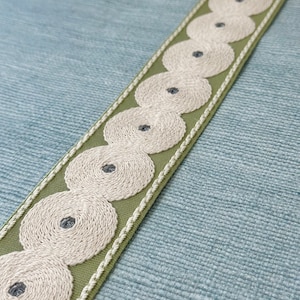 May include: Green fabric trim with white embroidered circles and a gray center. The trim has a stitched edge.