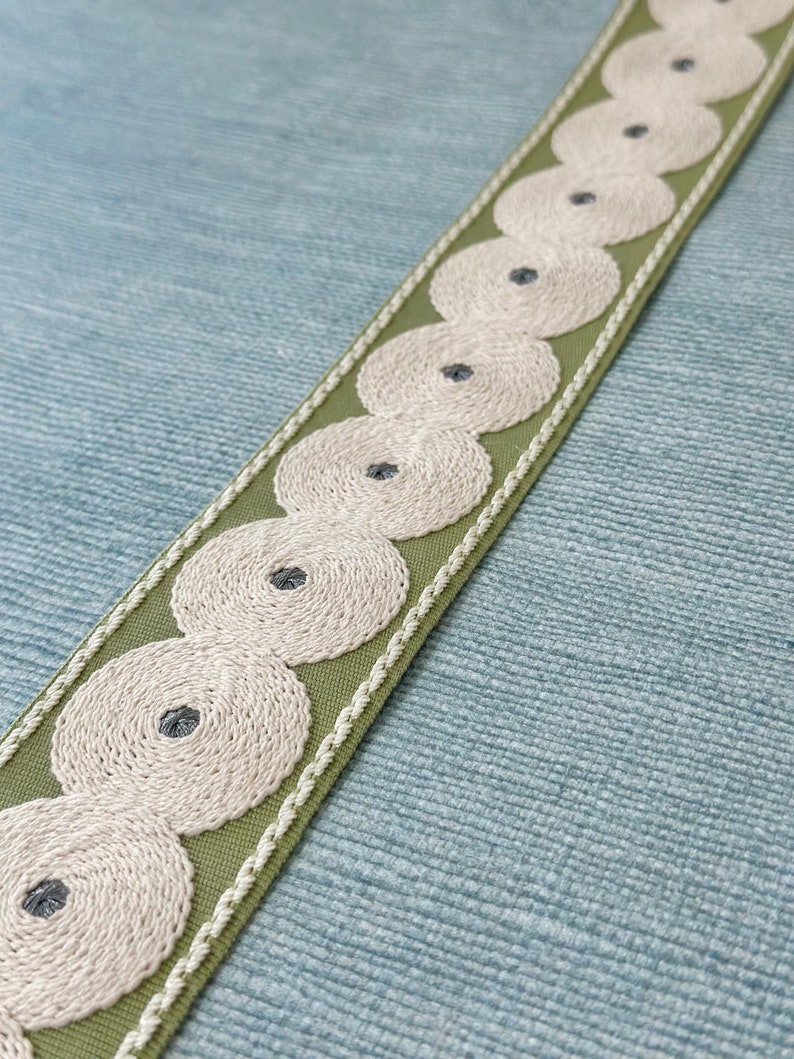 May include: Green fabric trim with white embroidered circles and a gray center. The trim has a stitched edge.