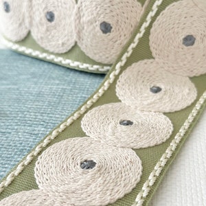 May include: Green fabric trim with a white embroidered design of concentric circles. The trim has a white edge.