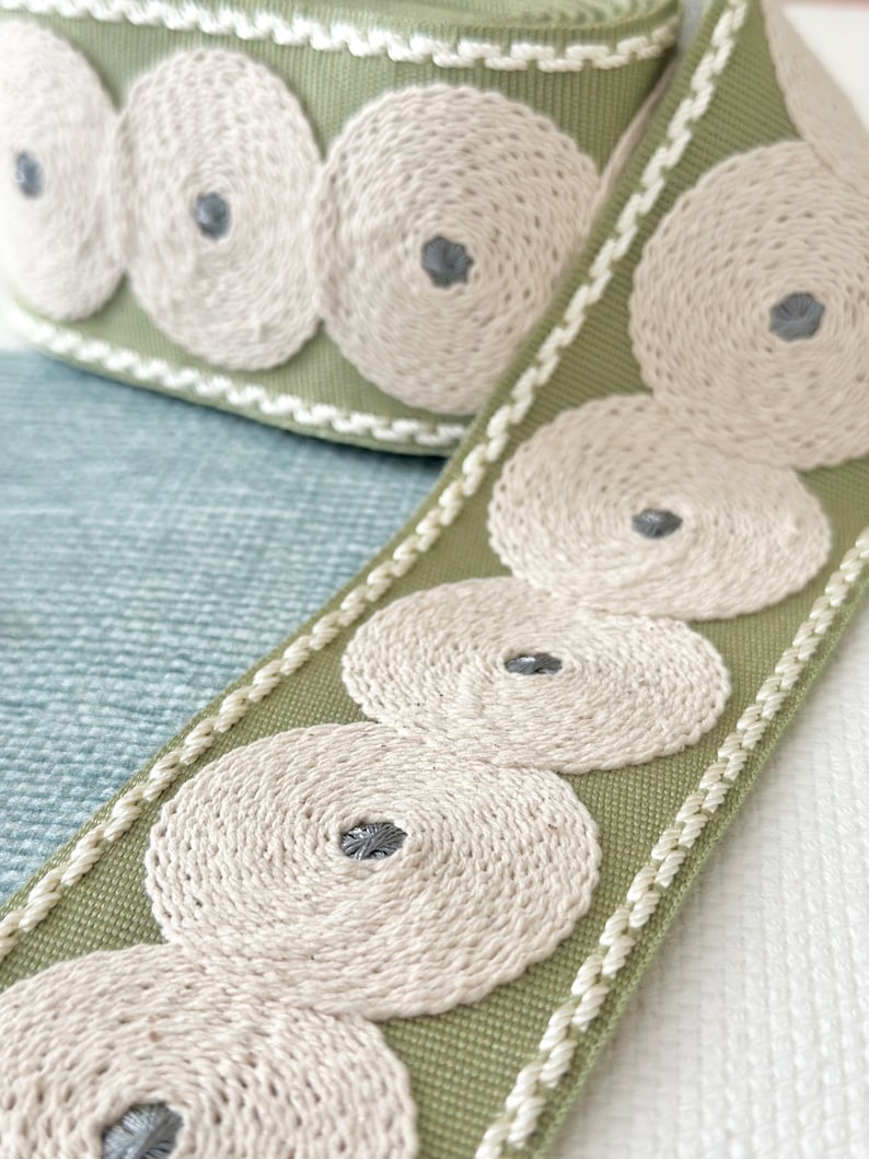 May include: Green fabric trim with a white embroidered design of concentric circles. The trim has a white edge.