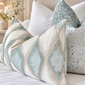 May include: A rectangular throw pillow featuring a textured diamond pattern in shades of light blue and cream. Beside it sits a square throw pillow in a light blue fabric with a metallic, speckled, and distressed-looking finish.