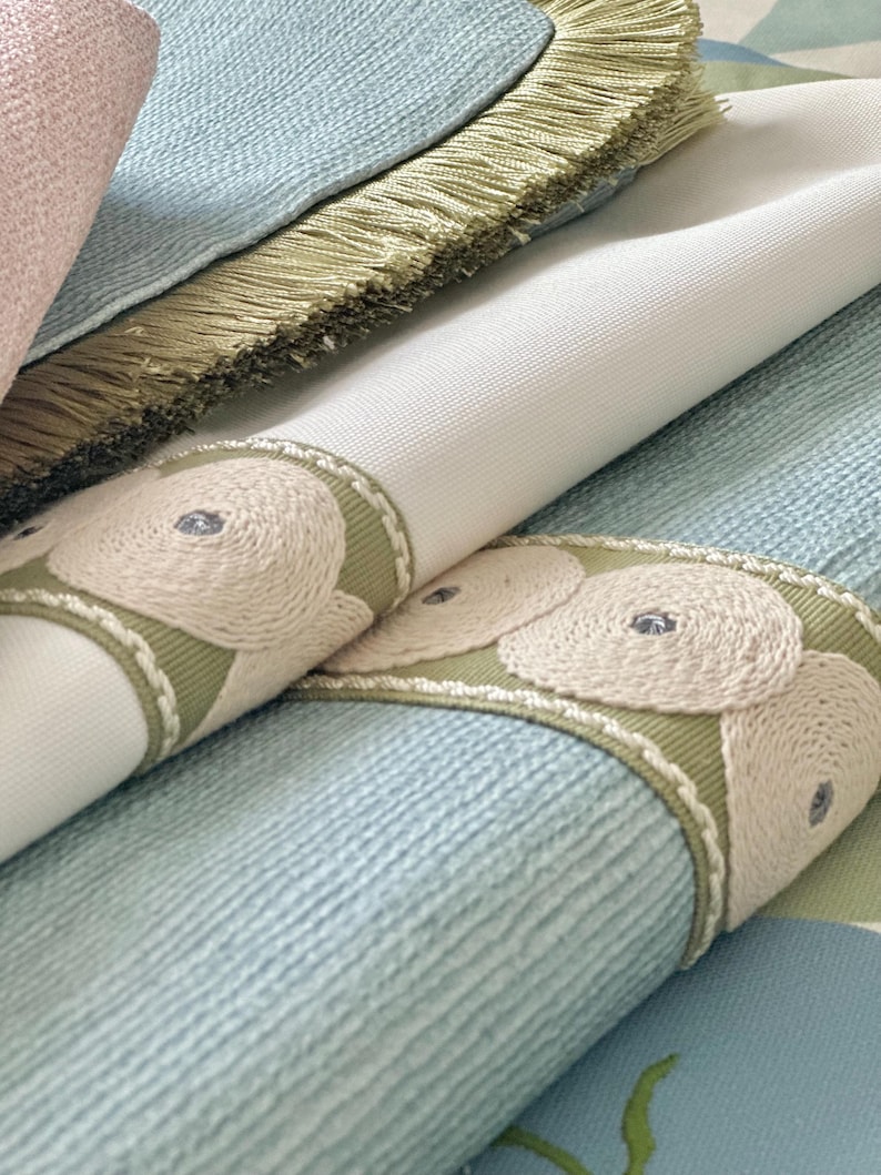 May include: Close-up of fabric swatches with a light blue, white, and green color scheme. The fabric has a textured surface and a decorative trim with embroidered circles.