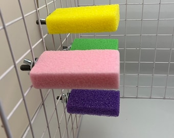 Puede incluir: Cuatro perchas rectangulares de color, esponjosas para animales pequeños, unidas a una jaula de alambre blanca con clips metálicos.