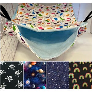 May include: A blue and white fabric hammock for small pets, with a dinosaur print on the outside and a soft blue fleece lining on the inside. The hammock is hanging from a white metal cage.