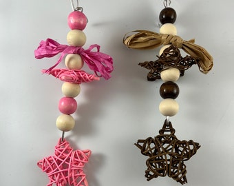 Puede incluir: Dos adornos de madera con cuentas y estrellas. El adorno de la izquierda tiene cuentas rosas y blancas con una estrella rosa. El adorno de la derecha tiene cuentas marrones y blancas con una estrella marrón.