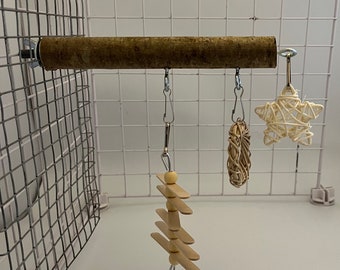 Op de afbeelding: Drie vogel speeltjes hangen aan een houten stok. De speeltjes zijn een geweven ster, een geweven bal en een houten ladder met kralen.