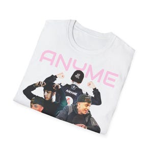 Puede incluir: Camiseta blanca con la palabra "ANYME" en rosa y un collage de fotos de cuatro personas. Las personas de la foto llevan chaquetas y gorras negras. La camiseta está doblada.