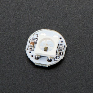 Könnte beinhalten: Eine kleine, runde, weiße Platine mit einer einzelnen, weißen LED-Leuchte. Die Platine hat mehrere kleine, schwarze Bauteile und den Text "CIC R1" aufgedruckt.