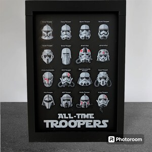 Può includere: Una stampa incorniciata nera con sfondo bianco e il testo "ALL-TIME TROOPERS" in basso. La stampa presenta 16 diversi elmetti di soldati di Star Wars in bianco e nero con accenti rossi.