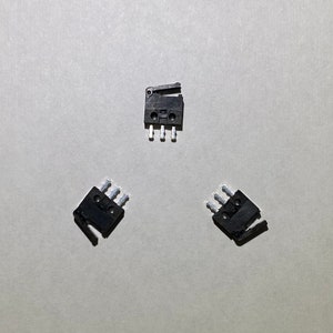 以下が含まれることがあります： 銀色の接点を持つ黒い電気スイッチが3つ。スイッチは白い背景に三角形の形で配置されています。