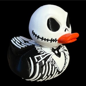 Puede incluir: Un patito de goma blanco y negro con pico naranja, diseñado para parecerse a Jack Skellington de Pesadilla antes de Navidad. El pato tiene una boca cosida y un diseño de esqueleto en el cuerpo.