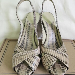 May include: A pair of open-toe slingback sandals with a snakeskin pattern in beige, brown, and black. The sandals feature a crisscross design and a thin ankle strap. The heels are approximately 7.6 cm high.