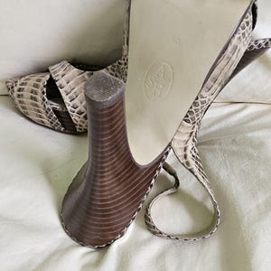 May include: Snakeskin-patterned high-heeled sandals in beige and brown. The sandals feature a chunky, brown heel and an ankle strap. The sole is marked with the size 40. The heels are approximately 10 cm high.