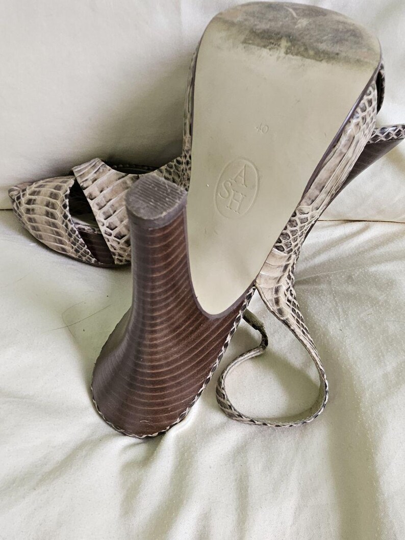 May include: Snakeskin-patterned high-heeled sandals in beige and brown. The sandals feature a chunky, brown heel and an ankle strap. The sole is marked with the size 40. The heels are approximately 10 cm high.