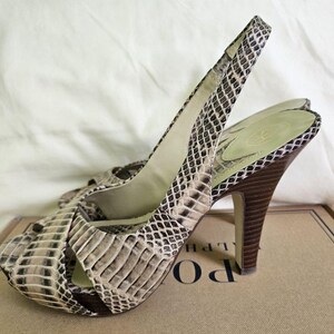 May include: Open-toe slingback heels with a snakeskin pattern in beige, brown, and black. The heels have a high, dark brown stiletto heel and an ankle strap. The heels are approximately 10 cm high.