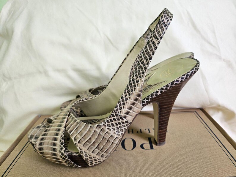 May include: Open-toe slingback heels with a snakeskin pattern in beige, brown, and black. The heels have a high, dark brown stiletto heel and an ankle strap. The heels are approximately 10 cm high.