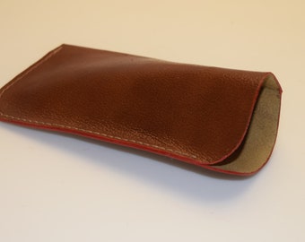 May include: A brown leather glasses case with a red stitched edge.