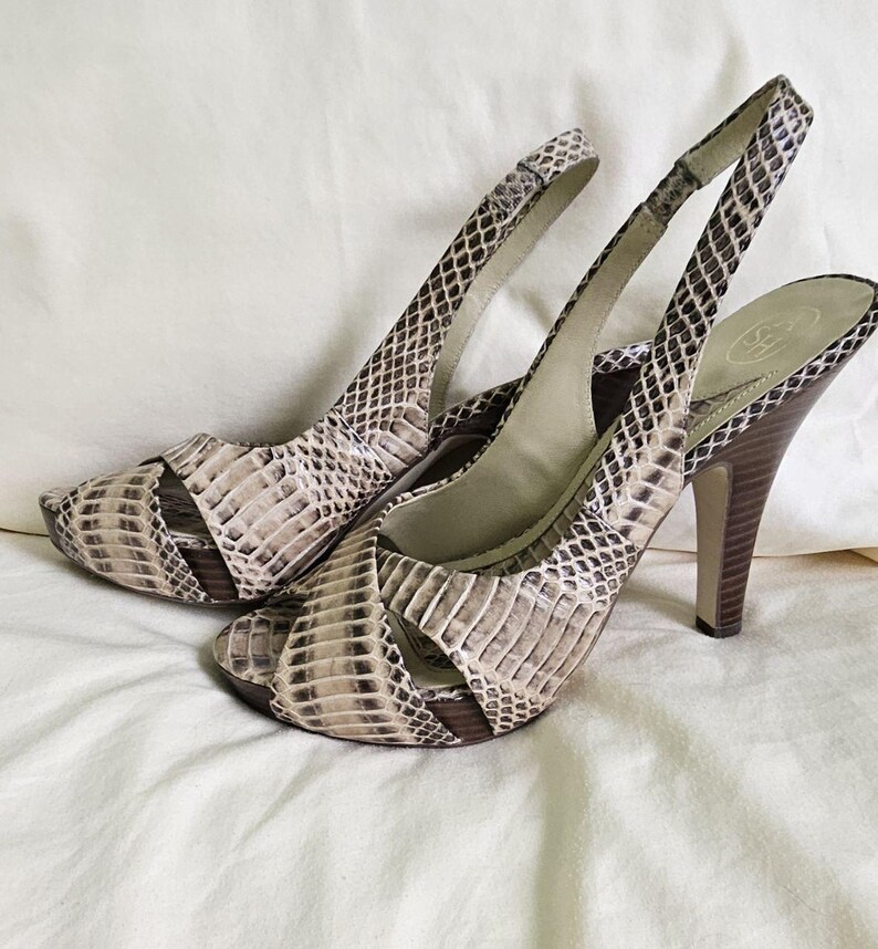 May include: A pair of high-heeled slingback sandals with a snakeskin pattern in beige, brown, and black. The heels are wooden, and the sandals have an open toe design.