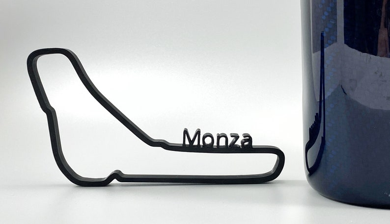 Może przedstawiać: Czarny zarys toru wyścigowego Monza z napisem "Monza" nadrukowanym na torze.