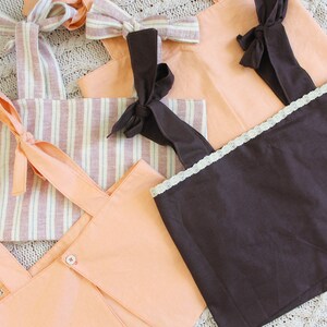 May include: Five different fabric tops with straps and bows. The tops are in shades of peach and brown. One top has a striped pattern.
