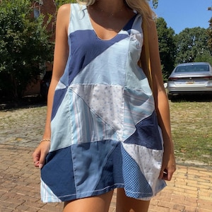 May include: A sleeveless patchwork dress in shades of blue, featuring a V-neckline. The dress is composed of various fabric patterns, including gingham, stripes, and polka dots. The dress is knee-length and appears to be handmade.