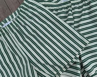 May include: Two pairs of green and white striped shorts. The shorts have an elastic waistband and a relaxed fit. The fabric features vertical stripes in a dark green color alternating with white stripes. The shorts are made of a lightweight material.