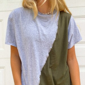 May include: A gray and olive green t-shirt with a unique diagonal color block design. The shirt has short sleeves and a crew neck. The two colors are separated by a raw edge seam.