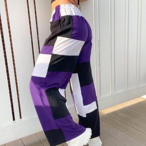 May include: Patchwork pants in a bold color block design. The pants feature large squares of purple, black, and white fabric. The waistline is elasticized. The pants are paired with white sneakers.