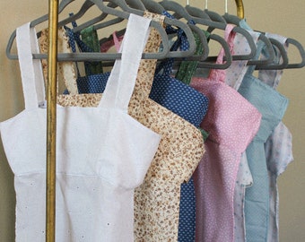 May include: A rack of clothing with a variety of patterns and colors. The clothing includes a white tank top, a floral print tank top, a blue and white patterned tank top, a pink tank top, and a light blue tank top.