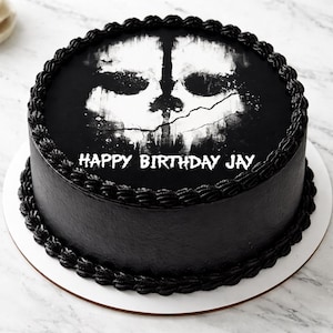 May include: A round, black frosted cake with a white skull graphic on top. The cake is decorated with black frosting around the edges and the words "HAPPY BIRTHDAY JAY" in white.