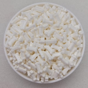 May include: A white bowl filled with white bone-shaped sprinkles. The sprinkles are small and have a slightly textured surface.