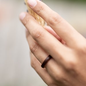 May include: A close-up of a hand wearing a dark brown ring. The ring is simple and elegant, with a smooth, polished finish.