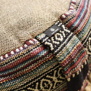 May include: Close-up of a round meditation cushion with a woven fabric top and a colorful patterned fabric bottom. The cushion has a black label with the text "Pure Creation" on it.