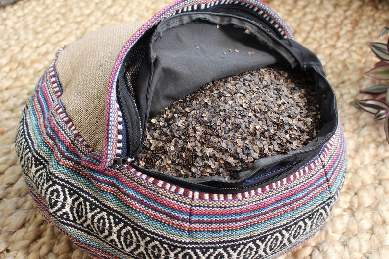 May include: A colorful, patterned meditation cushion filled with buckwheat hulls. The cushion is open, revealing the buckwheat hulls inside.