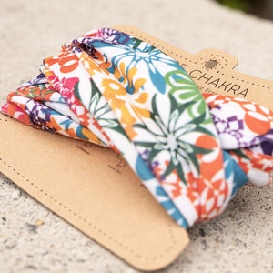 May include: A white headband with a colorful floral pattern. The headband is made of a soft, stretchy fabric and is perfect for keeping your hair out of your face. The headband is packaged in a brown cardboard box with the words "Chakra" and "Love Free" printed on it.
