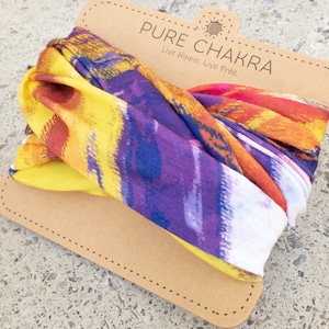 May include: A colorful, multi-colored fabric head wrap with a yellow, orange, purple, and white design. The fabric is folded and displayed on a brown card with the text "PURE CHAKRA Live Hippie. Live Free."
