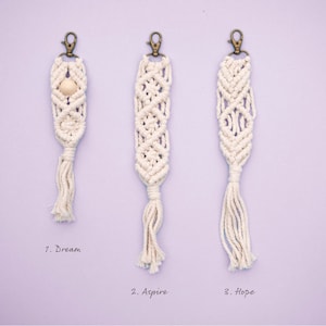 May include: Three white macrame keychains with a wooden bead on the first keychain. The keychains are labeled "1. Dream", "2. Aspire", and "3. Hope".