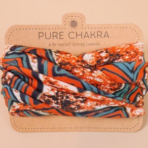 May include: A multi-colored fabric headband with a swirling pattern of orange, blue, and white. The headband is on a brown card with the text "PURE CHAKRA A Be Yourself Clothing Company".