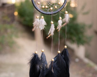 May include: A black dreamcatcher with gold beads and feathers. The feathers are black with gold tips.