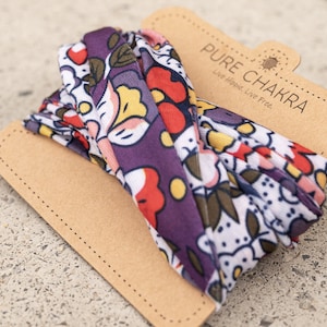 May include: A purple, white, red, and yellow floral patterned headband with the text "PURE CHAKRA Live Hippie Live Free" on a brown tag.