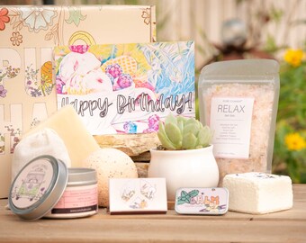 May include: A gift box filled with bath and body products, including bath salts, bath bombs, a candle, and a small succulent plant. The box is decorated with a floral pattern and the words "Happy Birthday!" are written on a card inside the box.