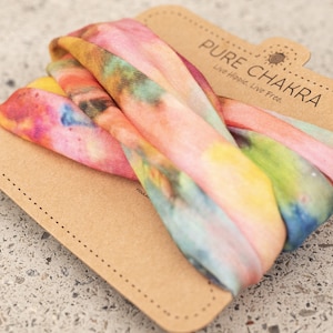 May include: A colorful tie-dye headband in shades of pink, yellow, blue, and green, resting on a brown cardboard tag. The tag features the text "PURE CHAKRA" and the tagline "Live Hippie, Live Free."