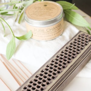 May include: A brown ceramic incense burner with a honeycomb design. The burner is sitting on a white surface with a small tin of soy wax candle that says "Pure Chakra" on the label.