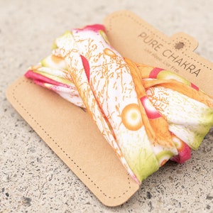 May include: A white, orange, and pink patterned fabric headband with the text "PURE CHAKRA Live Happy, Live Free." printed on a brown paper tag.